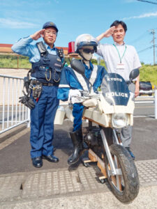 山家・口上林両地区を担当する綾部署山家駐在所（鷹栖町）の石川嘉孝巡査長（37）が、ドライバーに向け安全運転を啓発する「白バイかかし」を手作りした。秋の全国交通安全運動の期間中の25日、両地区を校区とする東綾小中一貫校（同町）に近い府道小浜綾部線沿いに設置した。